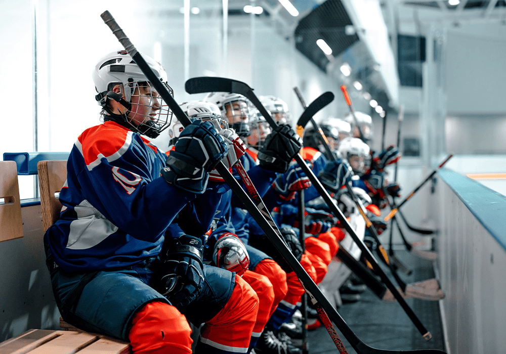 Members of a hockey team in a youth initiative sitting on the bench inside an ice rink.